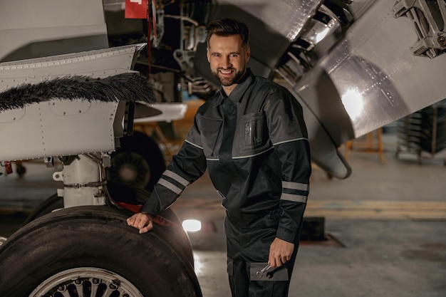 Mecánico de sexo masculino alegre que se coloca cerca del avión en hangar