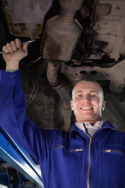 Mecánico sonriente mirando la cámara debajo de un coche