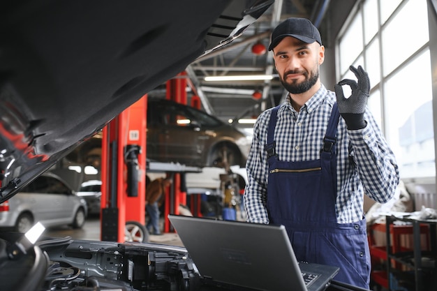 Mecánico sonriente usando una computadora portátil en el garaje de reparación