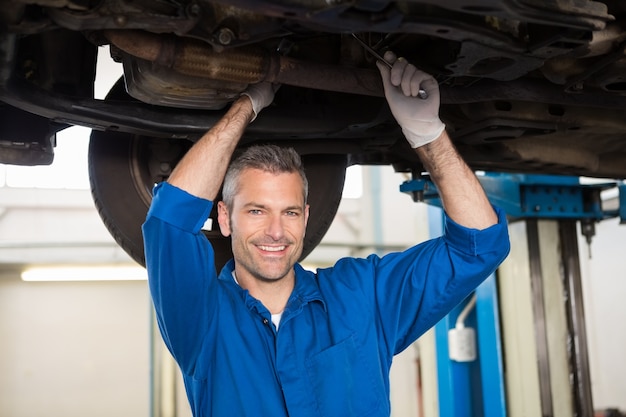 Mecânico sorrindo para a câmera sob o carro