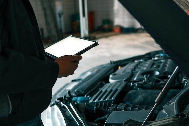 Un mecánico con una tableta mientras inspecciona un motor de automóvil en un taller Se centra en la integración de la tecnología moderna en el diagnóstico y la reparación de vehículos