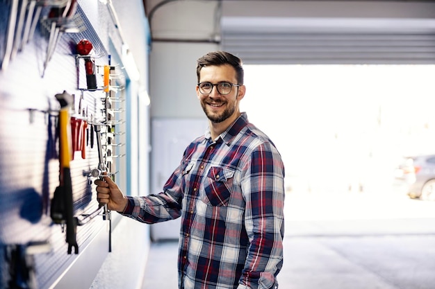 Un mecánico tomando la herramienta del tablero en el taller y sonriendo a la cámara