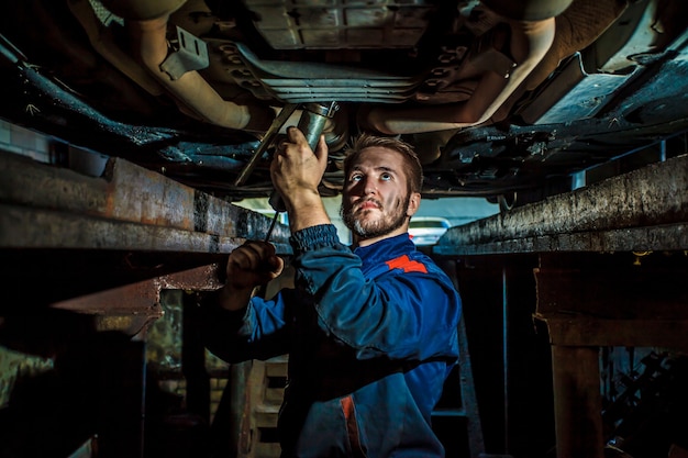 Mecánico en uniforme trabajando en auto servicio con vehículo elevado