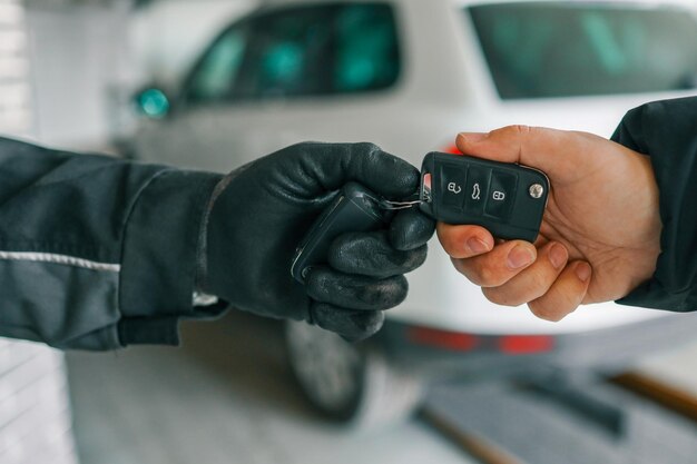 Mecânico usando luvas entregando chaves de carro a um cliente em uma oficina de reparo de automóveis com um carro branco ao fundo