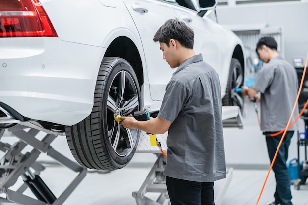 Mecánicos asiáticos revisando las ruedas del automóvil en el centro de servicio de mantenimiento