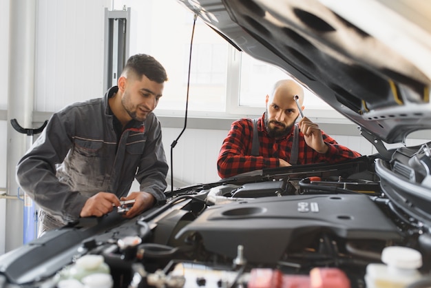 Mecânicos com chave inglesa consertando motor de carro na oficina