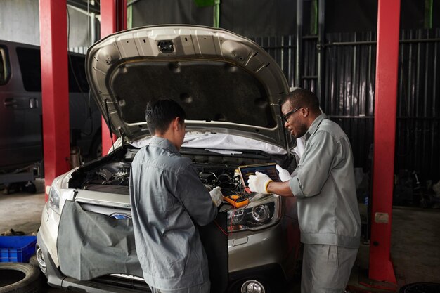 Mecánicos revisando el motor del automóvil con ayuda de una aplicación en una tableta