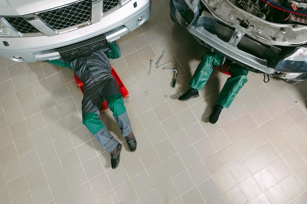 Mecánicos en uniforme acostados y trabajando debajo del coche en el garaje.