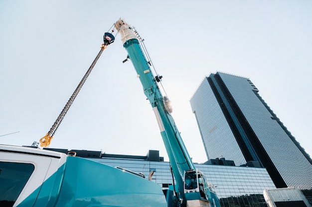 Mecanismo de elevación de grúa azul con ganchos cerca del edificio moderno de vidrio