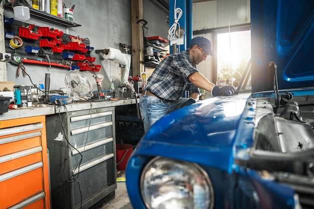 Mechaniker arbeitet tagsüber an einem klassischen blauen Auto in einer Garagenwerkstatt