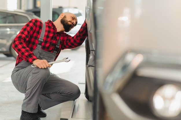 Foto mechaniker arbeitet und hält den schraubenschlüssel des serviceauftrags für die wartung des autos in der reparaturwerkstatt