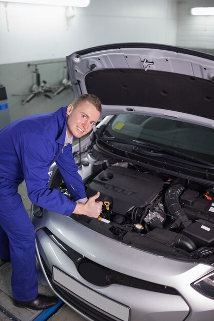 Mechaniker, der auf einem Auto beim Betrachten der Kamera sich lehnt