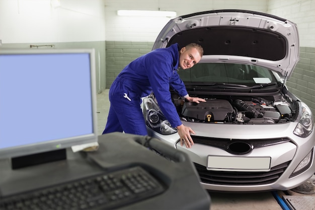 Mechaniker, der auf einem Auto nahe bei einem Computer sich lehnt