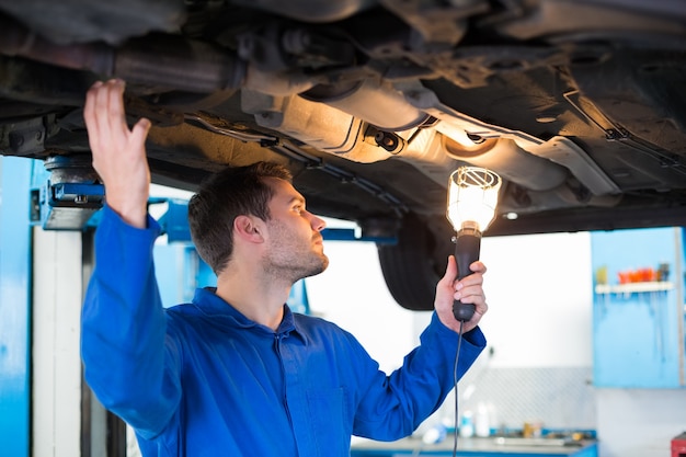 Mechaniker, der Fackel verwendet, um unter Auto zu schauen