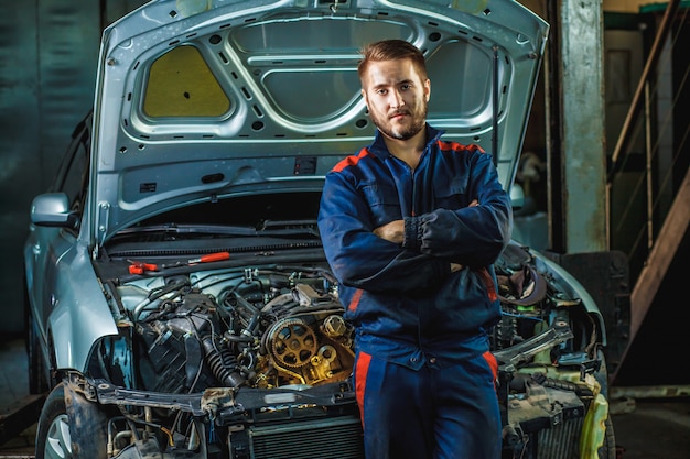 Mechaniker, der nahes Auto mit den gekreuzten Armen in der Garage steht.