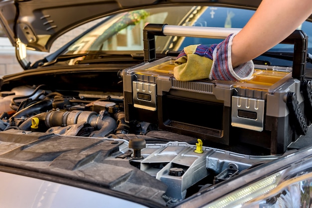 Mechaniker, der Werkzeugkasten nahe gebrochenem Auto hält