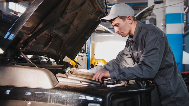 Mechaniker in der Autowerkstatt, die die Motordiagnose in der Motorhaube des Autos bearbeitet