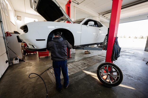 Mechaniker in der Service-Reparaturstation, die mit Muscle-Car arbeitet, zerlegt ein Rad auf der Hebebühne