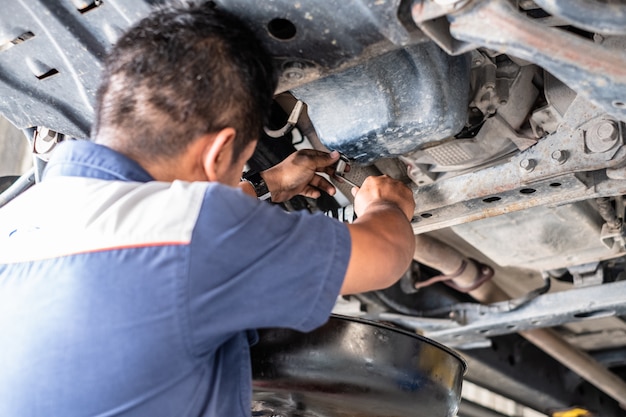 Mechaniker Mann reparieren Auto in der Garage und Motoröl wechseln. Er stand unter dem Auto an der Aufzugsmaschine.