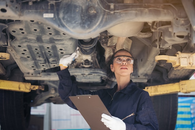 Mechanikerin, die ein angehobenes Auto inspiziert