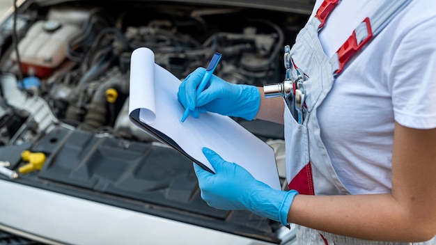 Mechanikerin steht mit einem Tablet mit einer Liste von Pannen am Fahrgestell eines Autos