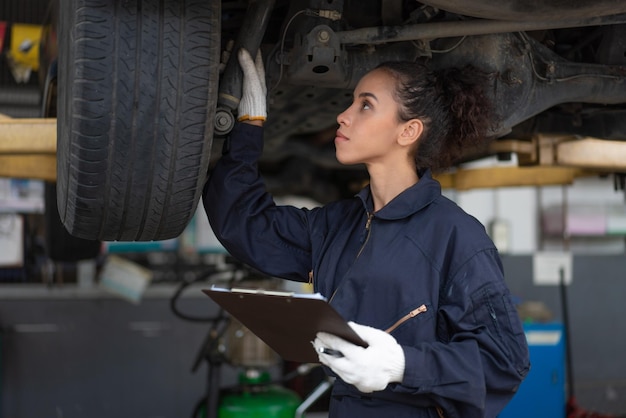 Mechanikerin überprüft und repariert das Reifenrad unter dem Fahrzeug im Auto in der Garage