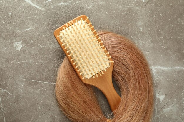 Un mechón de cabello femenino con cepillo sobre fondo de textura gris