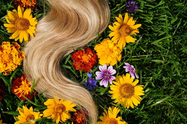 Un mechón de cabello rubio entre las flores en la hierba verde concepto de salud del cabello ingrediente natural cos ...