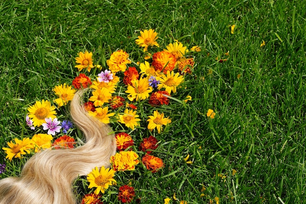 Un mechón de cabello rubio entre las flores en la hierba verde concepto de salud del cabello ingrediente natural cos ...