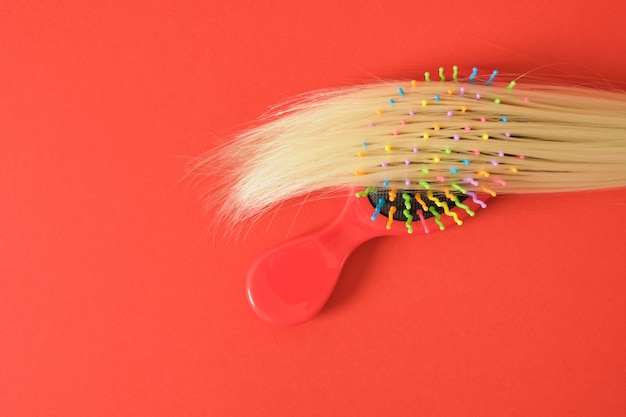 Un mechón de cabello rubio y un peine de masaje de plástico rojo sobre un fondo rojo espacio de copia concepto de pérdida de cabello cuidado del cabello y aumento del crecimiento del cabello