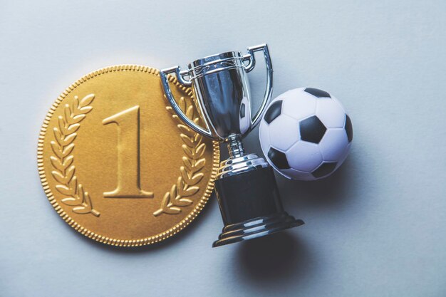 Foto medalha e troféu dos vencedores do primeiro lugar de ouro com uma bola de futebol conceito de conquista de sucesso de futebol