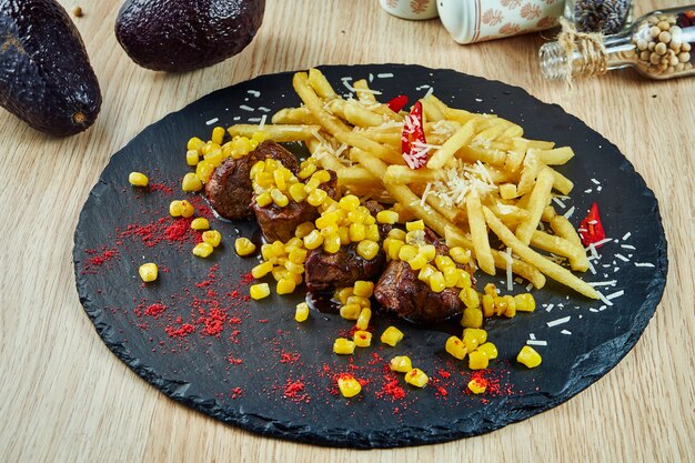 Medalhões de bife de vitela assada com batatas fritas e milho em uma placa de ardósia preta. Fast-food americano clássico. Alimentos ricos em calorias e gorduras. Close-up de comida saborosa