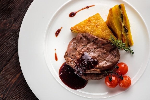 Medalhões de carne com molho de bagas e torta de batata em um prato branco, vista superior