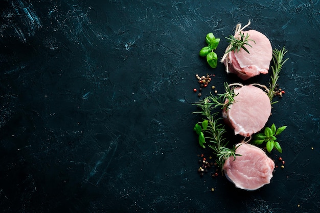 Medalhões de carne crua com alecrim e especiarias Em um fundo de pedra preta Vista superior Espaço para cópia grátis