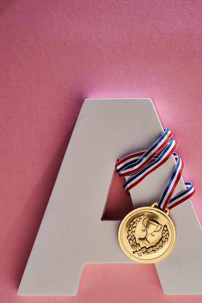 Medalla de oro y alfabeto a sobre fondo rosa