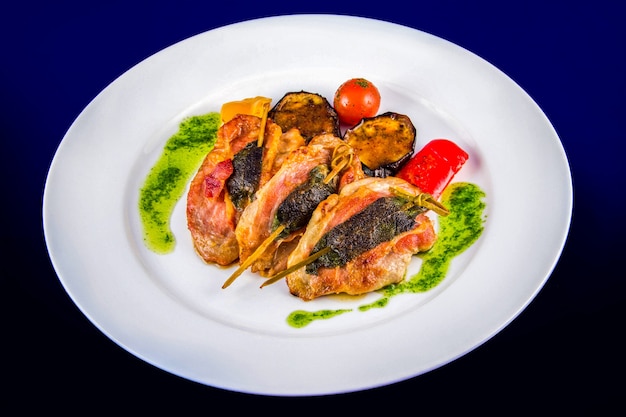 Medallones de pavo rellenos de hierbas en brochetas con verduras a la plancha y salsa pesto. Vista superior plana laicos sobre un plato blanco sobre un fondo azul.