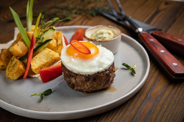 Medallones de ternera con huevo, patatas y pimientos en una mesa de madera