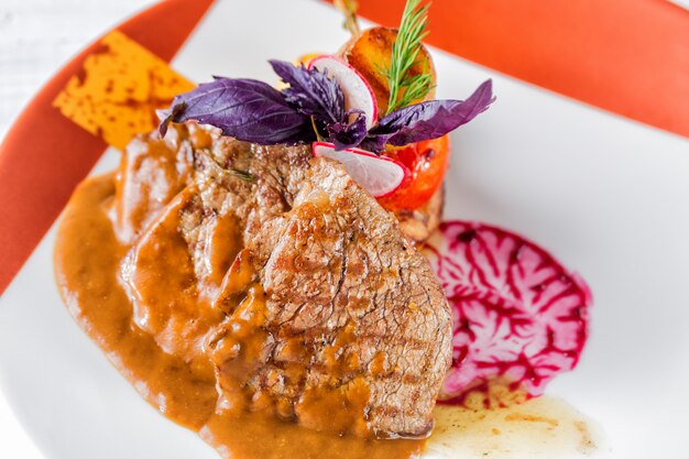 Medallones de ternera con salsa, decorados con rábano, tomate, berenjena y hierbas