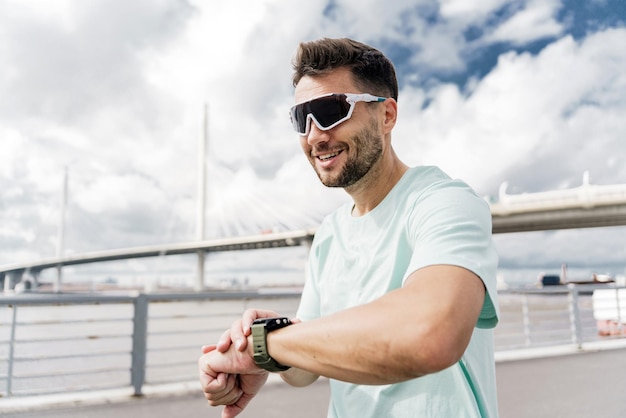 Mede o tempo com óculos de desporto usa uma aplicação e um relógio de fitness no braço Treinador de corrida Homem de fitness