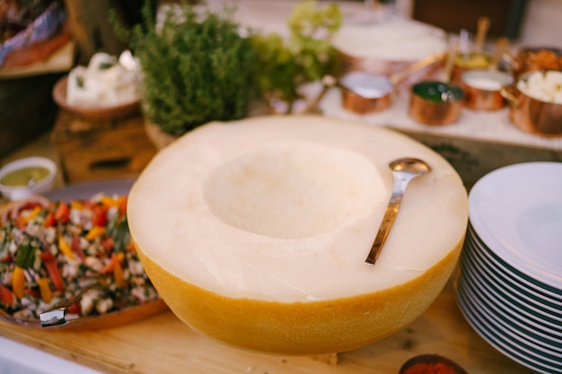 Media bola de queso sobre una mesa de madera con platos de cuchara y ensalada en un plato de queso parmesano duro