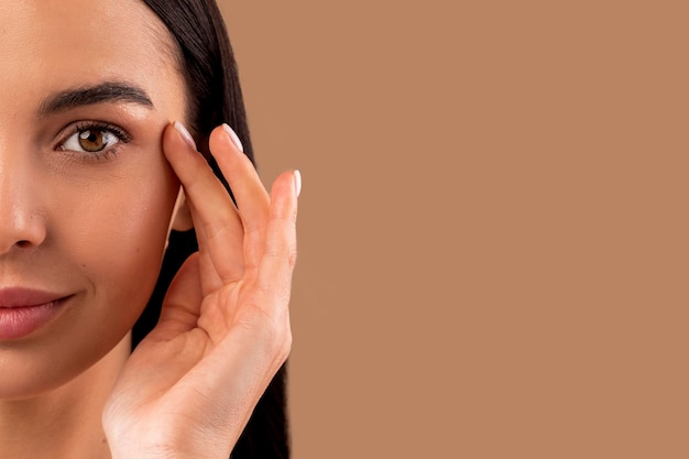 Media cara de mujer morena atractiva tocando debajo de la piel de los ojos