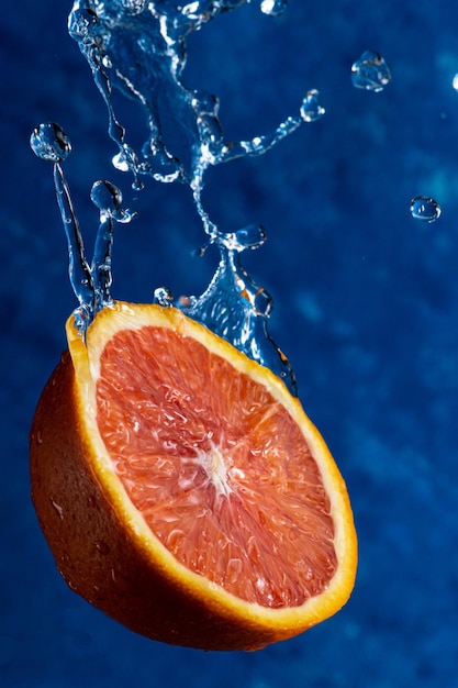Media naranja cae sobre un fondo azul con gotas de agua