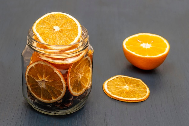 Media naranja fresca sobre la mesa Rodajas de naranja secas y conos de abeto en un frasco
