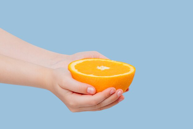 Media naranja recortada en manos de niña aislada en azul