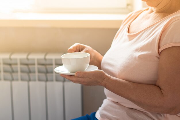 Mediados de mujer adulta que bebe el café y que mira fuera de la ventana en día asoleado. Sha horizontal