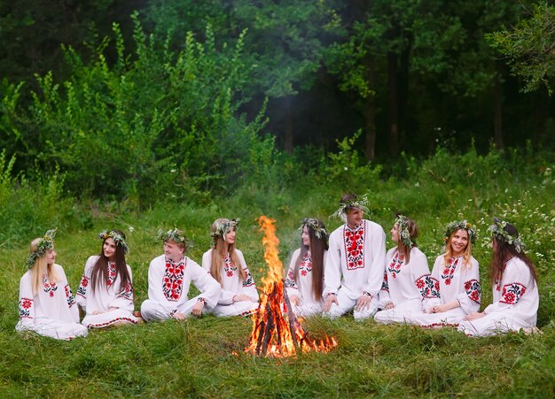 A mediados del verano, jóvenes con ropa eslava sentados en el bosque cerca del fuego.