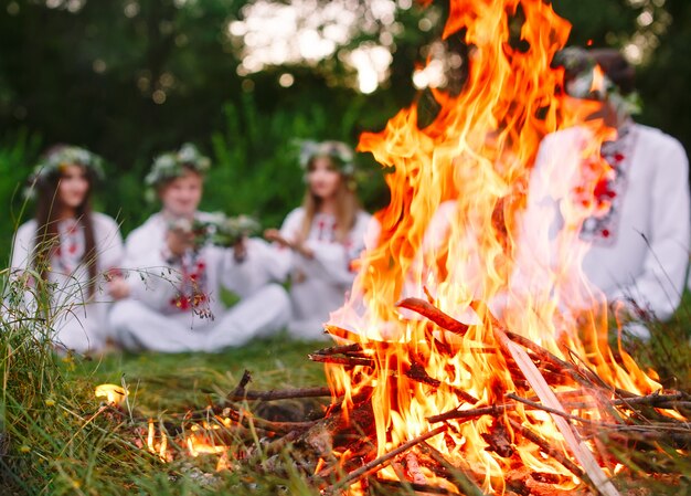 A mediados del verano, jóvenes con ropa eslava sentados en el bosque cerca del fuego.