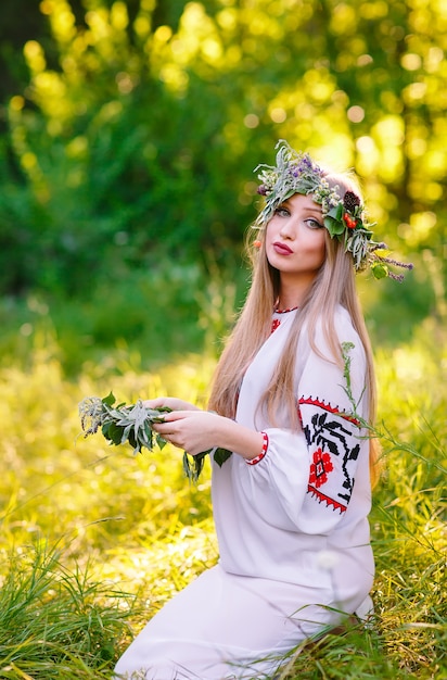 A mediados del verano, mujer tejiendo una corona de flores cerca del fuego.