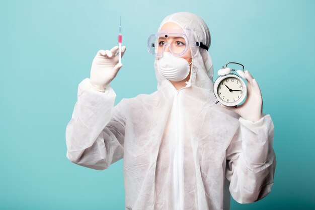 Medic mujer vestida con ropa protectora contra el virus con jeringa y reloj despertador
