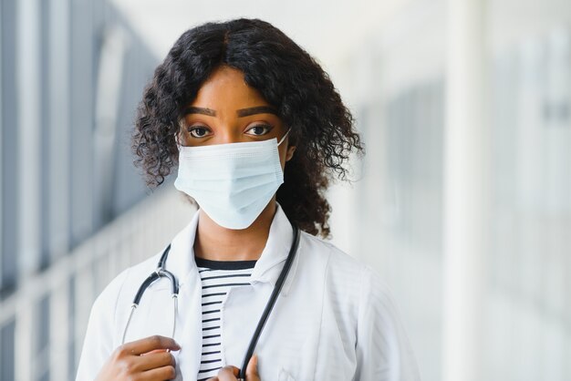 Médica africana americana feminina, mulher enfermeira vestindo jaleco com estetoscópio e máscara. feliz, animado para o trabalhador médico de sucesso posando sobre fundo claro. conceito de pandemia, covid 19